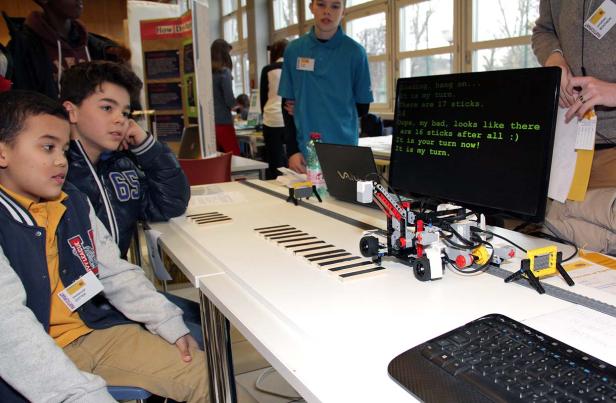 Zwei Jungen beobachten einen Roboter, der über eine Strecke mit Holzstäben fährt.