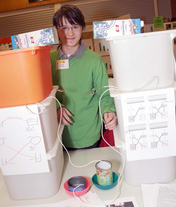 Ein Jugendlicher präsentiert ein wissenschaftliches Projekt mit Behältern, Dosen und Milchpackungen.