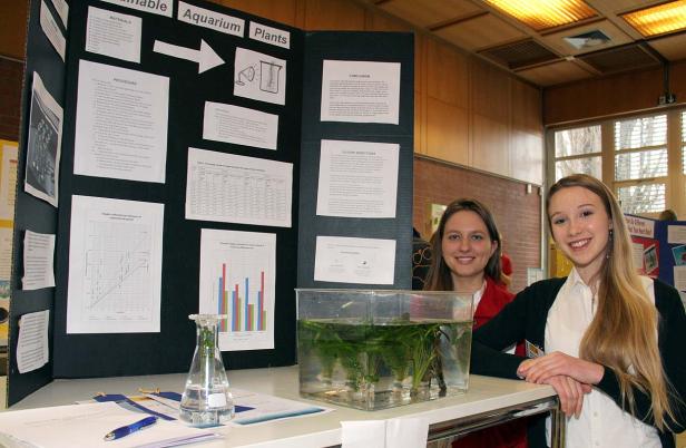 Zwei junge Frauen präsentieren ein Projekt über Wasserpflanzen in einem Aquarium.