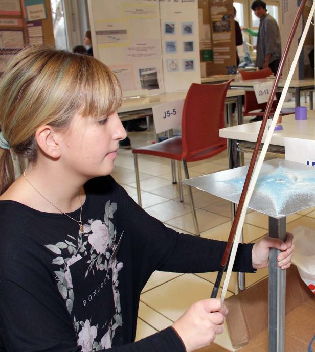 Ein junges Mädchen führt ein Experiment mit einer Geige und Sand durch.