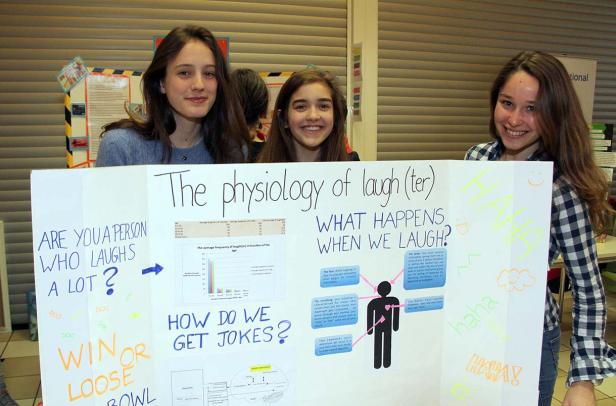 Drei junge Frauen präsentieren eine Schautafel zum Thema „Die Physiologie des Lachens“.