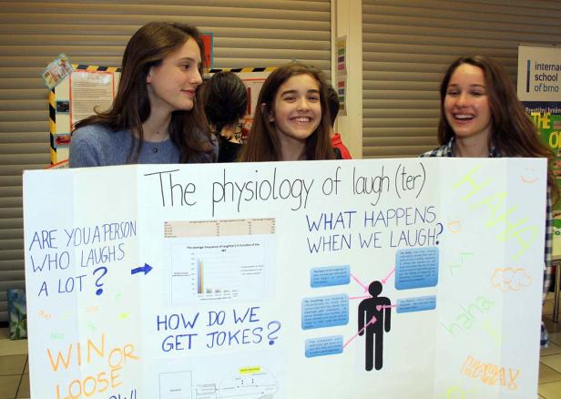 Drei junge Frauen präsentieren eine Schautafel über die Physiologie des Lachens.