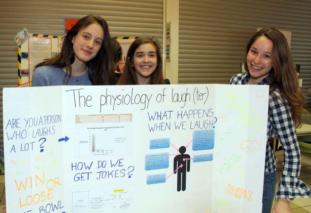 Drei junge Frauen präsentieren eine Schautafel über die Physiologie des Lachens.