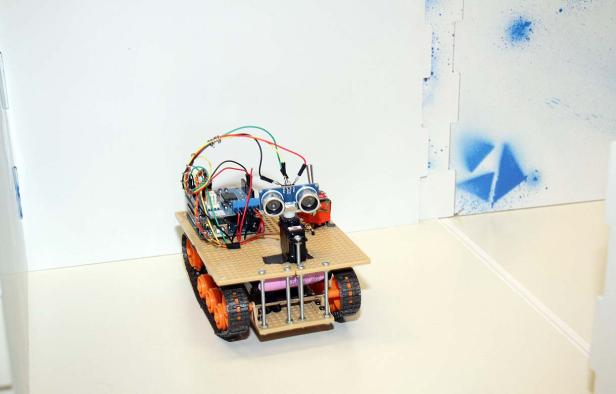 Ein kleiner Roboter mit Raupenantrieb und elektronischen Bauteilen steht auf einem Tisch.