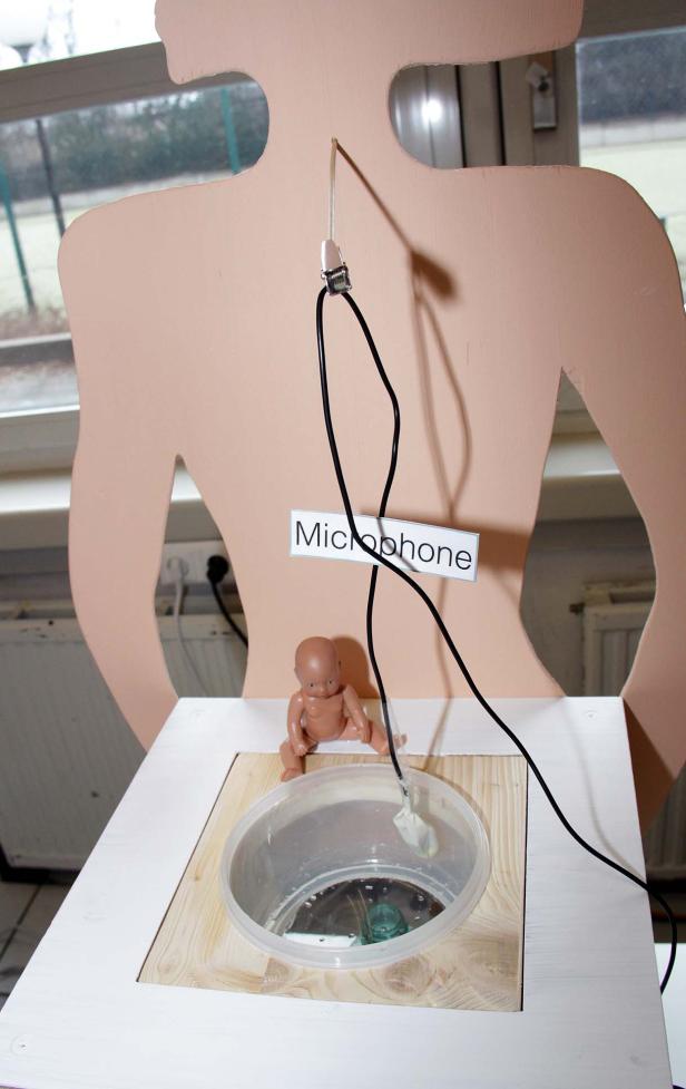 Eine Installation mit einer Puppe, einem Mikrofon und einem Behälter mit Wasser.