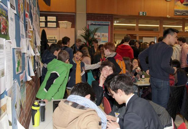 Eine Gruppe von Schülern steht und sitzt in einem belebten Innenraum.