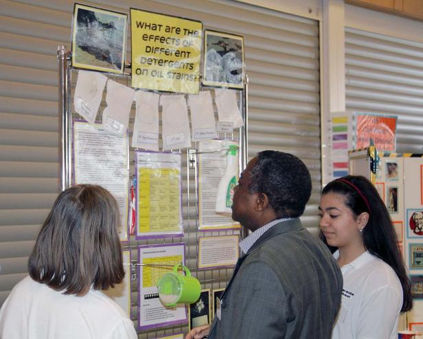 Eine Frau, ein Mann und ein Mädchen betrachten eine Präsentation über die Wirkung von Reinigungsmitteln auf Ölflecken.