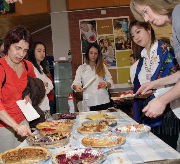 Menschen stehen an einem Tisch mit verschiedenen Kuchen und probieren diese.