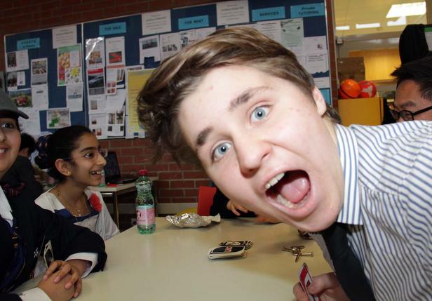 Eine Gruppe von Schülern sitzt an einem Tisch, ein Junge schaut mit offenem Mund in die Kamera.