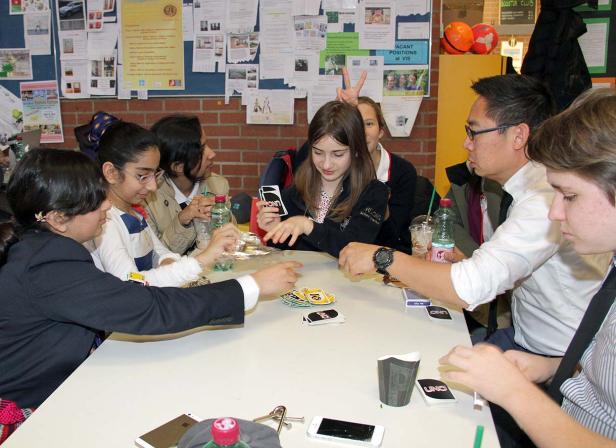 Eine Gruppe von Schülern und ein Lehrer spielen Uno an einem Tisch.