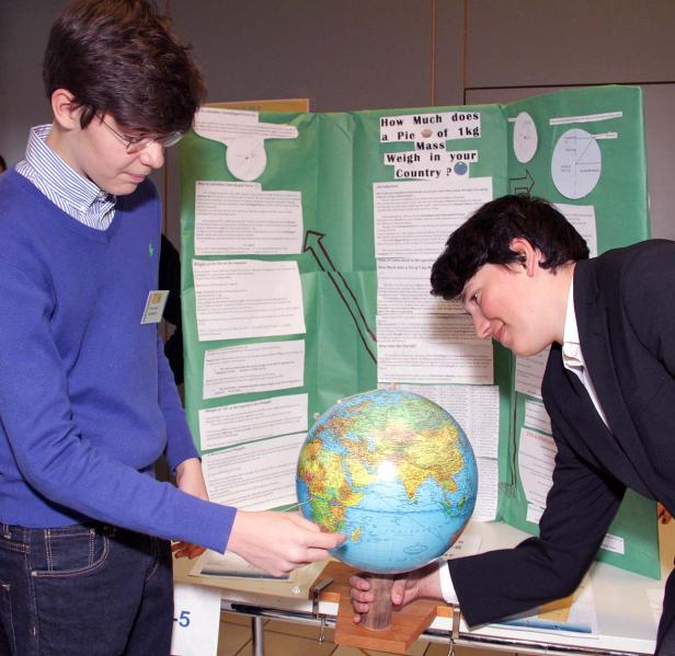 Zwei Jugendliche präsentieren ein Projekt über das Gewicht eines Kuchens in verschiedenen Ländern anhand einer Weltkugel.