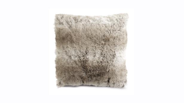 Ein quadratisches Kissen mit einem Bezug aus Kunstfell in Grau- und Beigetönen.