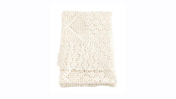 Eine gefaltete, gehäkelte, cremefarbene Decke auf einem weißen Hintergrund.