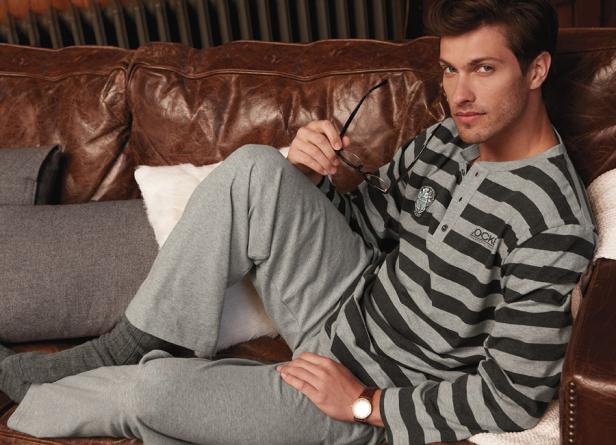 Ein Mann in grau gestreifter Loungewear entspannt auf einem Ledersofa.