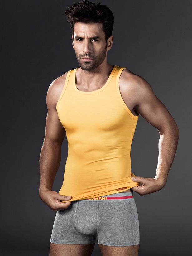 Ein Mann mit Bart trägt ein gelbes Unterhemd und graue Boxershorts.