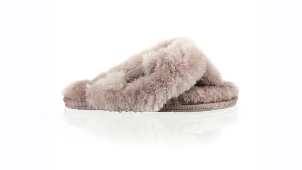 Ein beiger, flauschiger Hausschuh mit gekreuzten Riemen steht auf einem weißen Hintergrund.