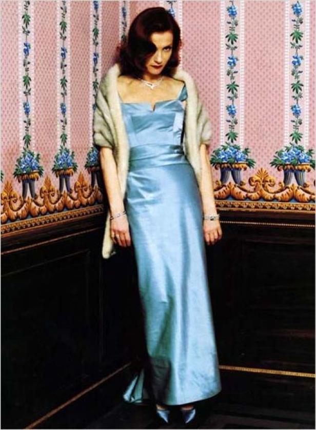 Eine Frau in einem hellblauen Kleid und einer Stola posiert vor einer floralen Tapete.