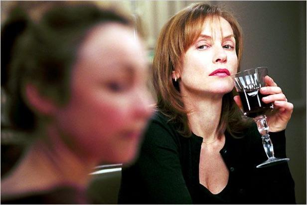 Isabelle Huppert hält ein Glas Rotwein in der Hand.