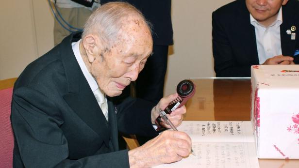 Ein älterer Mann unterschreibt ein Dokument mit einem Stift und hält einen Stempel in der Hand.