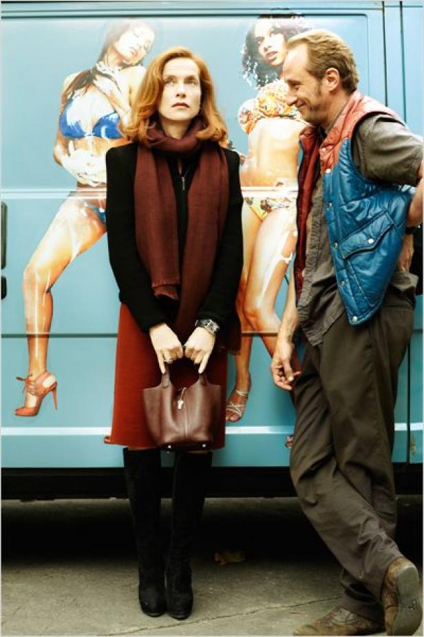Isabelle Huppert und ein Mann stehen vor einem Bus mit aufgemalten Frauen im Bikini.