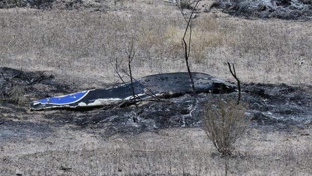 Ein zerstörtes Flugzeugwrack liegt in einem abgebrannten Feld.