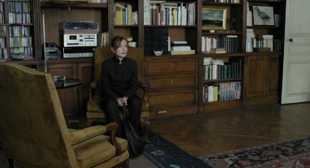 Isabelle Huppert sitzt in einem Sessel vor einem Bücherregal.