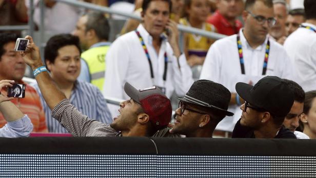 Mehrere Personen, darunter Neymar und Dani Alves, schauen ein Sportereignis und machen Fotos.
