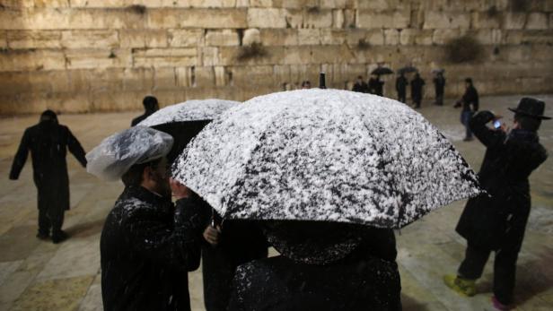 Jüdische Menschen stehen im Schnee vor der Klagemauer in Jerusalem.