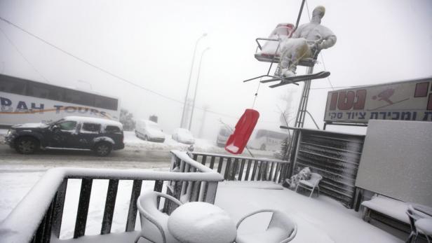 Verschneite Straßenszene mit Autos, einem Bus und einer Skilift-Dekoration im Nebel.