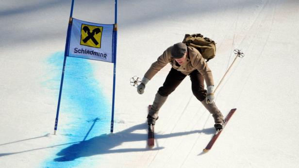 Ein Skifahrer in traditioneller Kleidung fährt an einem Tor in Schladming vorbei.