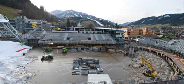Bauarbeiten an einer Sportanlage in einer Stadt vor einer Bergkulisse.
