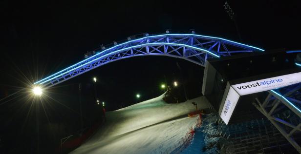 Eine Skipiste bei Nacht mit blauer Beleuchtung und dem Logo von Voestalpine.