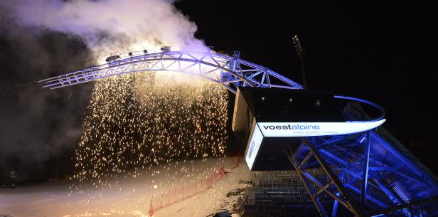 Feuerwerk erhellt eine Skipiste neben einer Struktur mit der Aufschrift „voestalpine“.