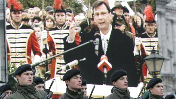 Soldaten stehen vor einer Leinwand, auf der ein Mann eine Rede hält.