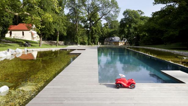 Ein rotes Bobby-Car steht auf einem Holzsteg an einem Schwimmteich.