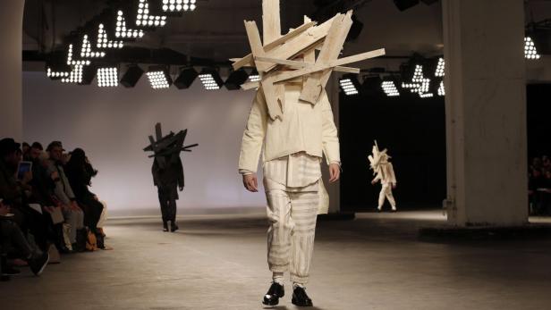 Ein Model mit einer Kopfbedeckung aus Holz auf einem Laufsteg.