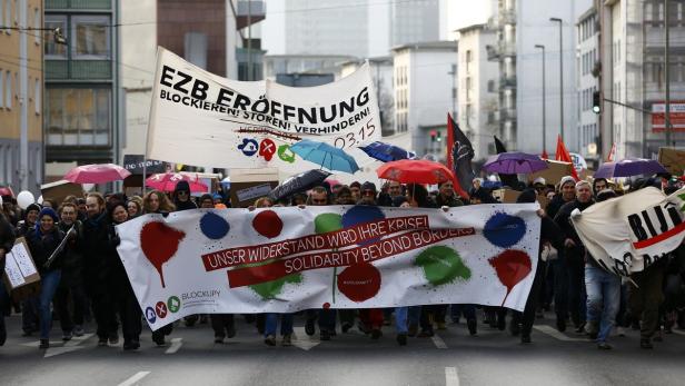 Eine Demonstration gegen die EZB-Eröffnung mit Transparenten und Regenschirmen in Frankfurt.