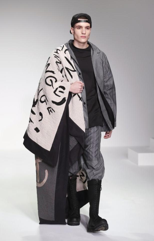 Ein Mann in einem gestreiften Anzug und Stiefeln trägt einen gemusterten Überwurf.