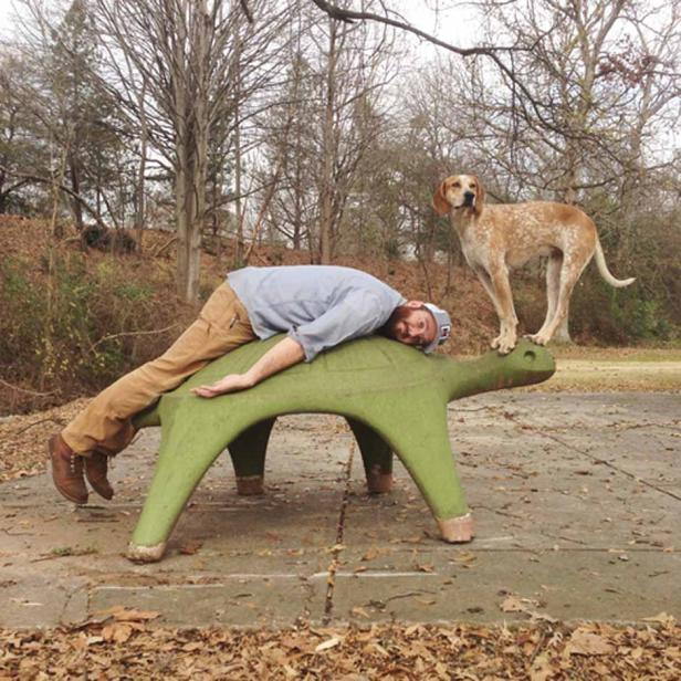 Ein Mann liegt auf einer grünen Schildkrötenskulptur, während ein Hund auf ihrem Kopf steht.