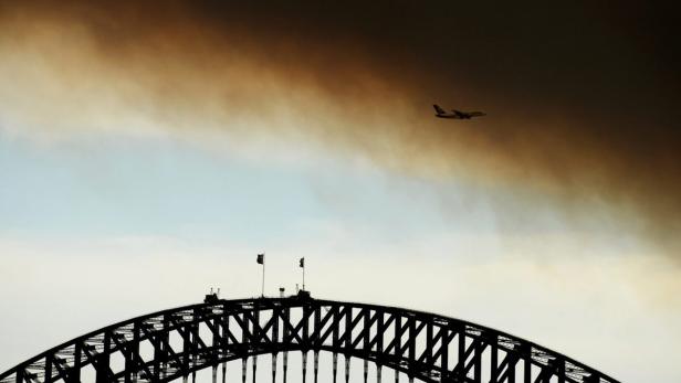 Ein Flugzeug fliegt über die Silhouette der Sydney Harbour Bridge.