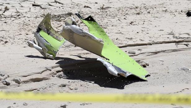 Trümmerteile eines Flugzeugs liegen auf sandigem Untergrund.