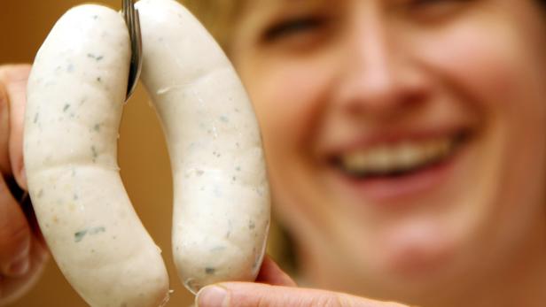 Eine Frau hält mit einer Gabel zwei Weißwürste hoch.