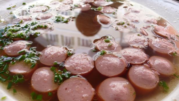 Eine Schüssel mit Wurstscheiben in Brühe, garniert mit Schnittlauch.