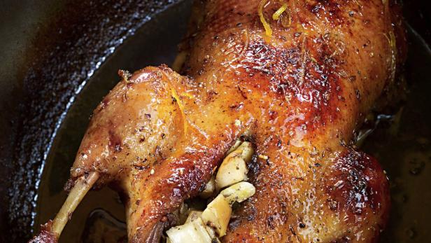 Ein gebratener Truthahn mit glänzender Haut und Kräutern in einer dunklen Pfanne.