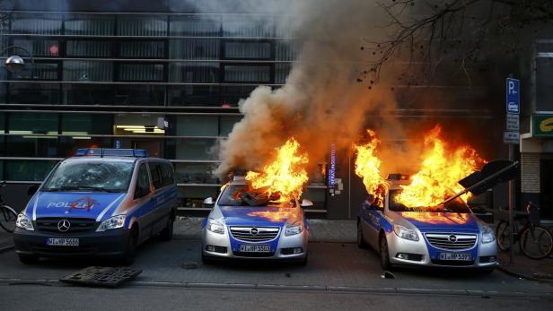 Mehrere brennende Polizeiautos stehen vor einem Gebäude.
