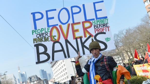 Ein Demonstrant hält ein Schild mit der Aufschrift „People over Banks“ in die Höhe.