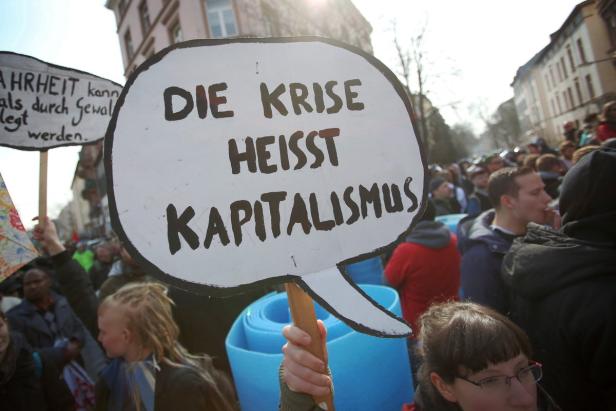 Demonstranten halten Schilder mit der Aufschrift „Die Krise heißt Kapitalismus“.