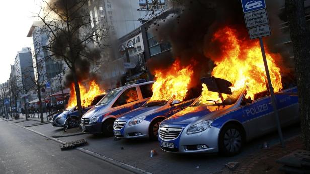 Mehrere brennende Polizeiautos stehen am Straßenrand.