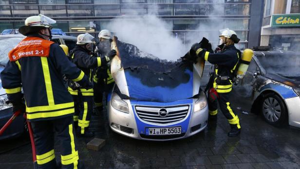 Feuerwehrleute löschen einen brennenden Opel-Polizeiwagen.