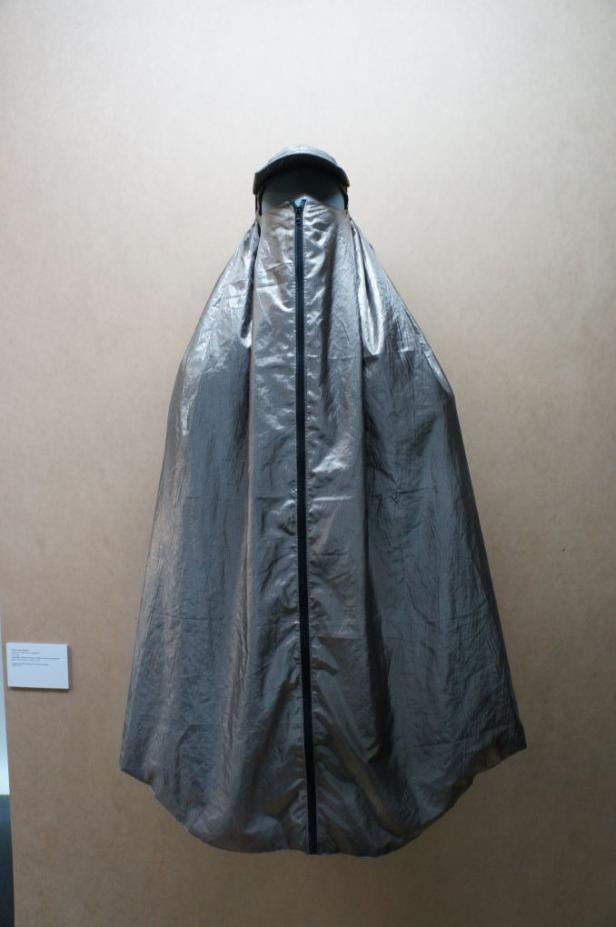 Eine silberfarbene Burka mit Reißverschluss hängt an einer Wand.